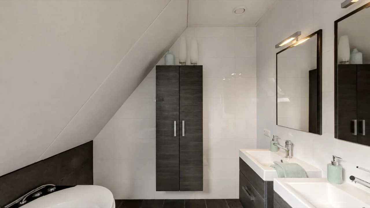 Badkamer met dubbele wastafel en een bad onder het schuine dak in Damwoude